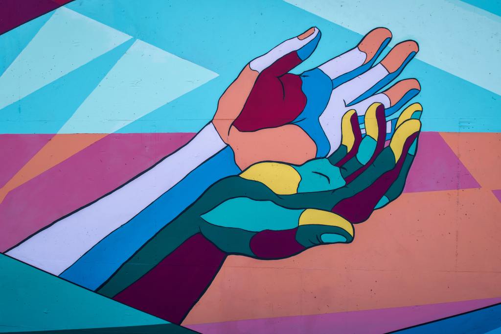 Colourful mural of two open, cupped hands, one resting in the other, painted in blocks of blue, pink, yellow and teal